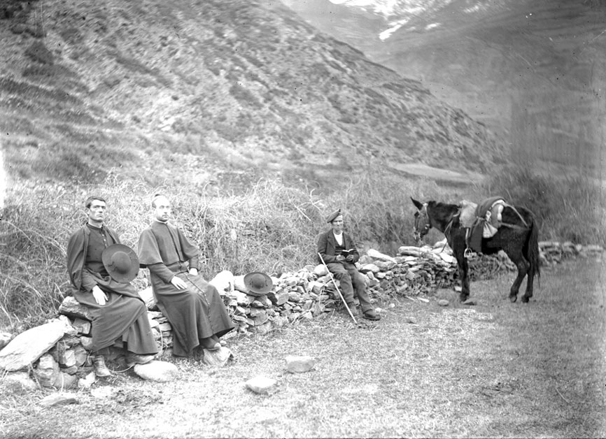 <p>Un parell de sacerdots descansa a la vora del camí, durant trajecte cap a Escalarre, mentre el traginer, vora del matxo, llegeix tranquil·lament.</p>